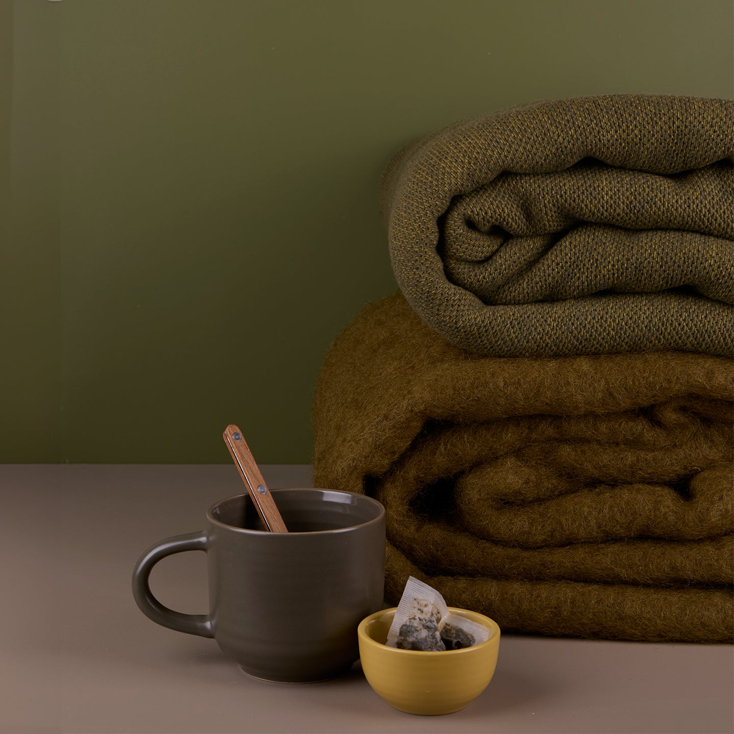 Stack of mohair and wool throws alongside a mug full of tea.