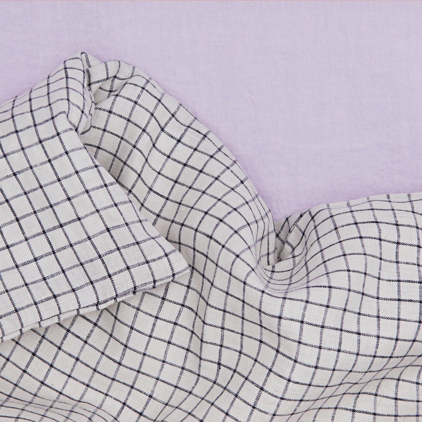 A close up of a checked linen duvet cover on a lilac sheet.