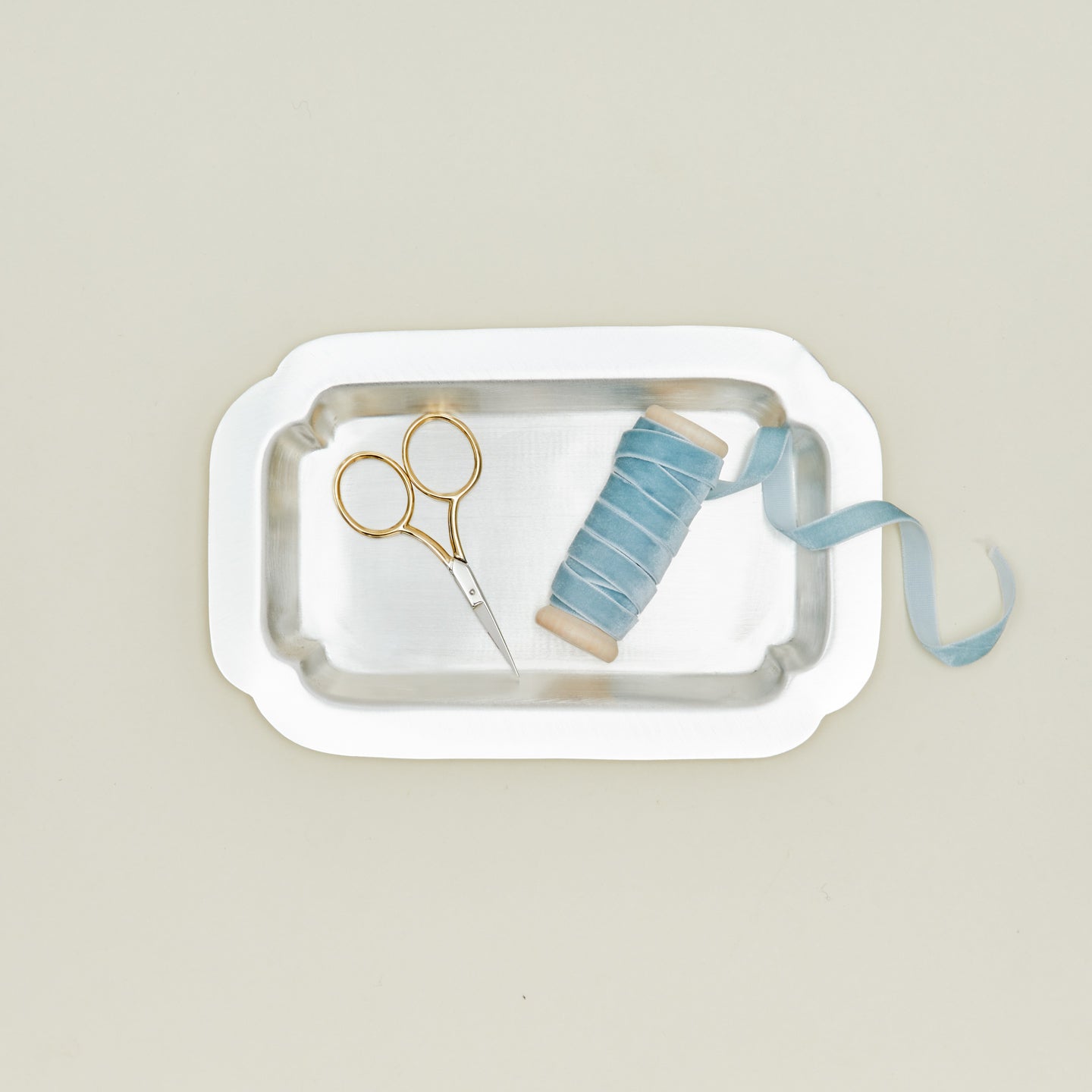 Overhead view of decorative edge rectangular silver tray with a spool of velvet ribbon, and gold handled ribbon scissors