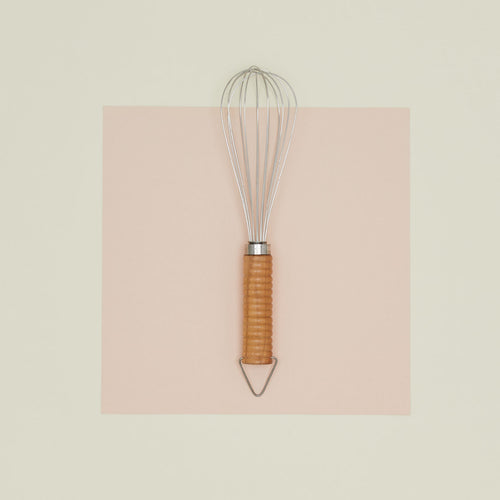 Stainless steel whisk with wooden handle on paper.