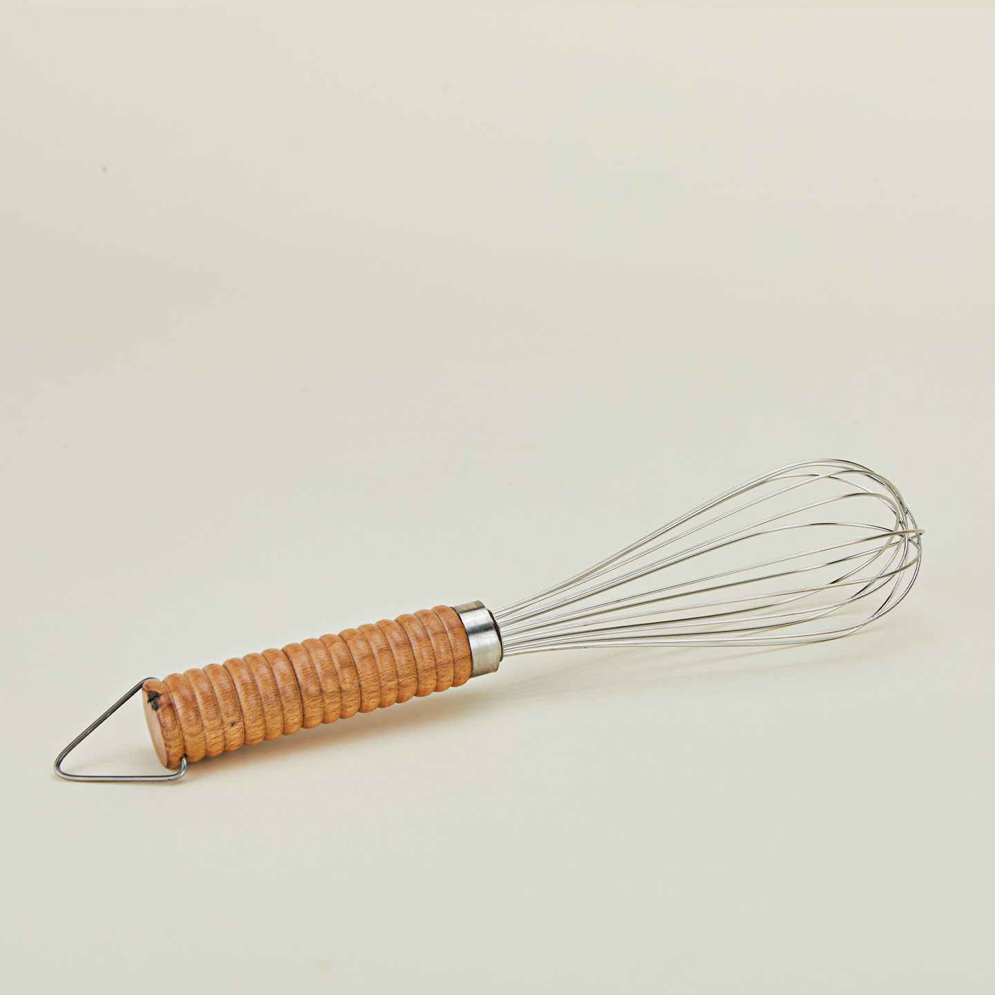 Close up of stainless steel whisk with wooden handle.