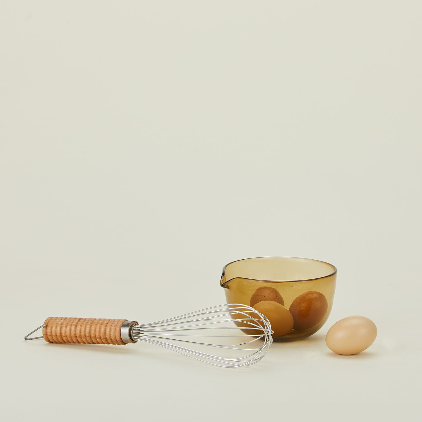 Stainless steel whisk with wooden handle and bowl of eggs.