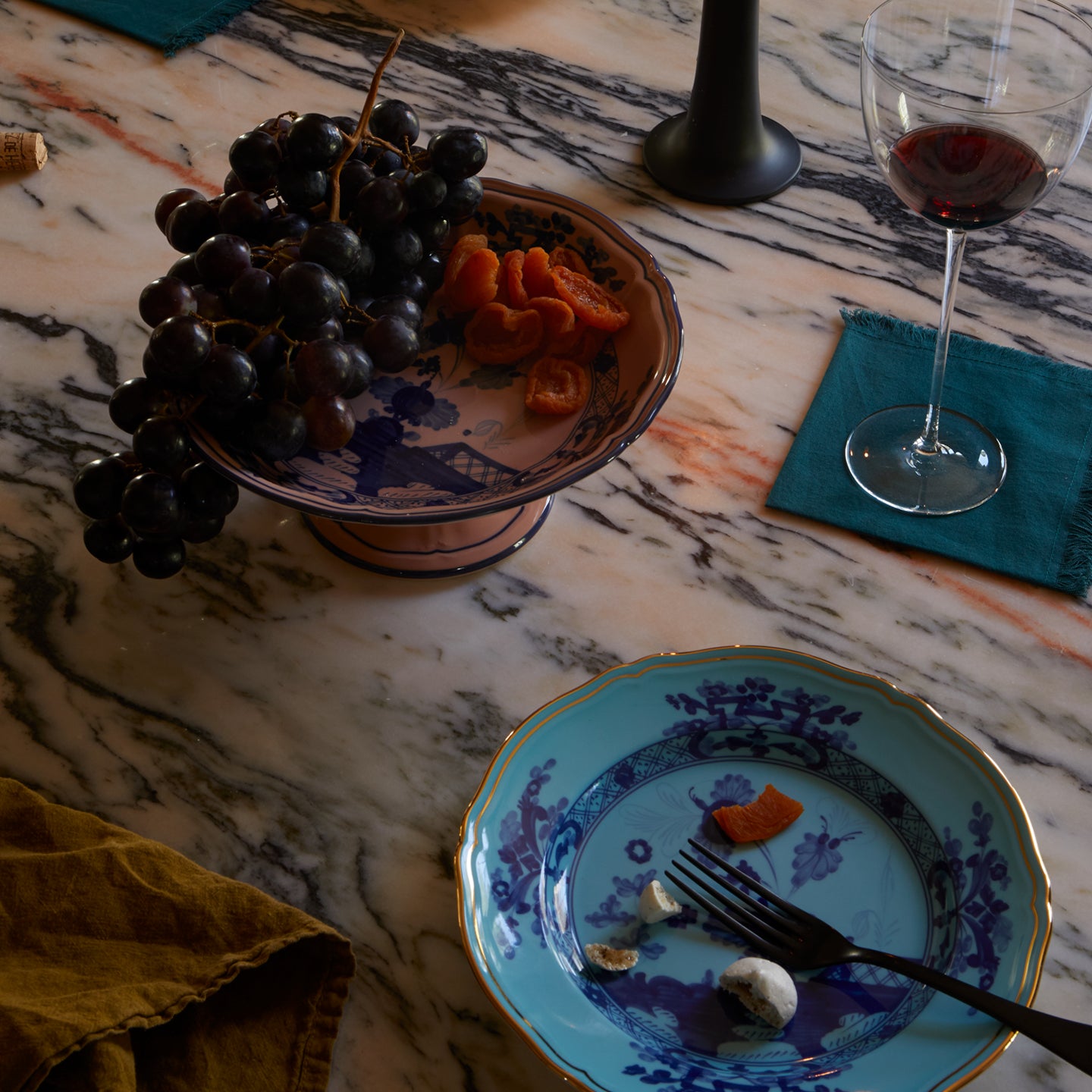 Marble table set with wine glasses, cloth napkins, candlelight and Ginori porcleain pieces with floral motifs and gold accents.