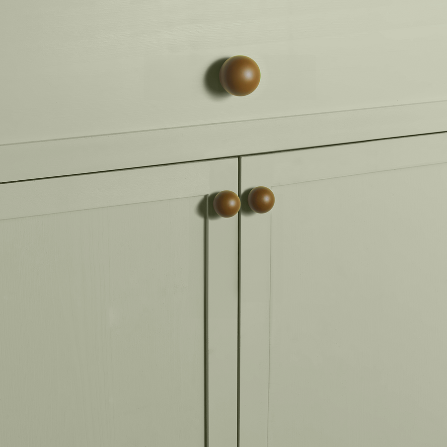 Close-up of olive green spherical knobs on sage green cabinets.