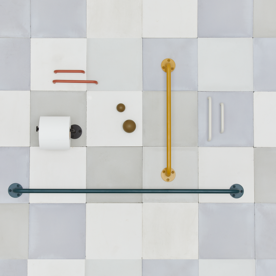 Essential hardware pieces including knobs, pulls, towel bars, and toilet paper holders in various colors arranged on a background of grey tile.