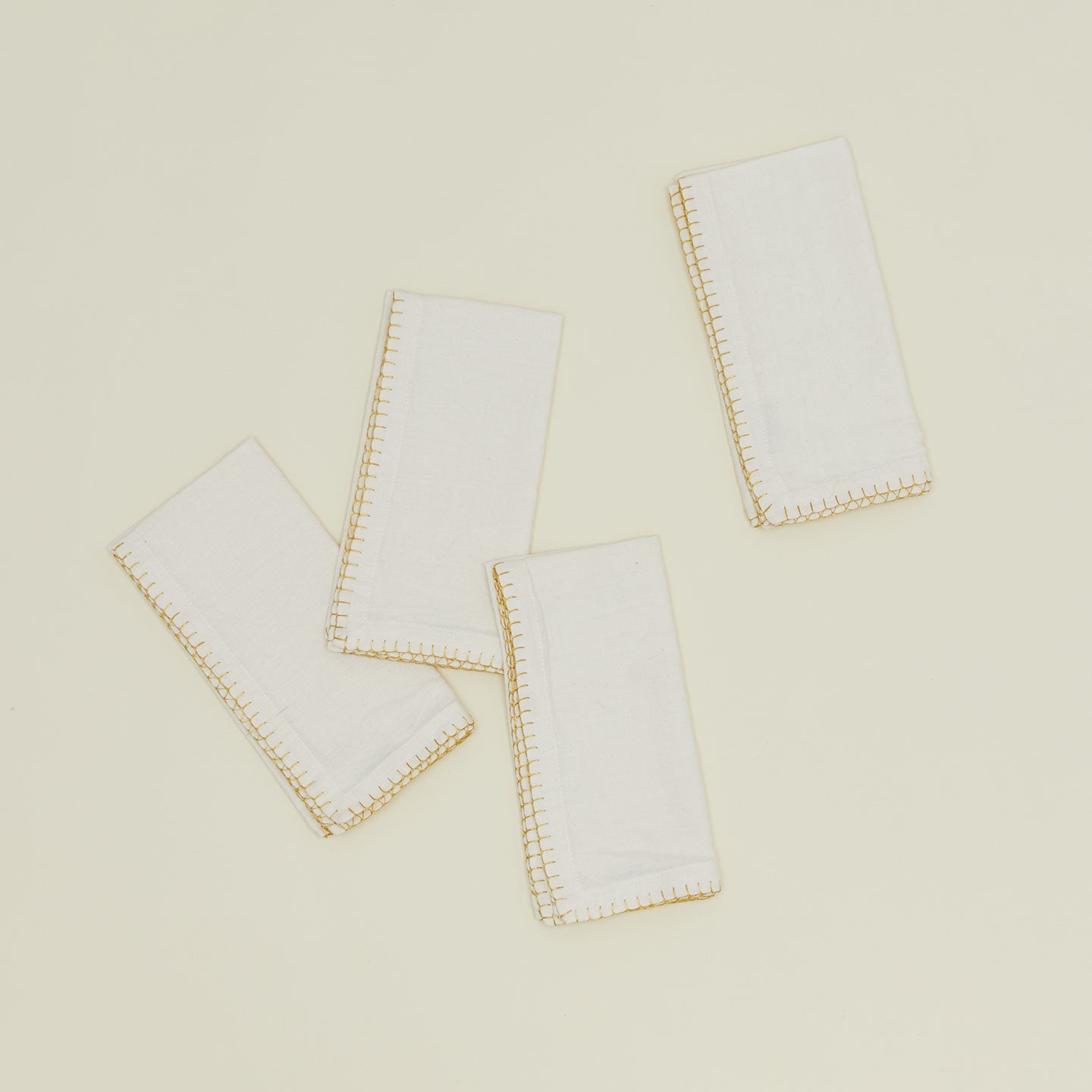 A set of four ivory napkins with gold blanket stitching. 