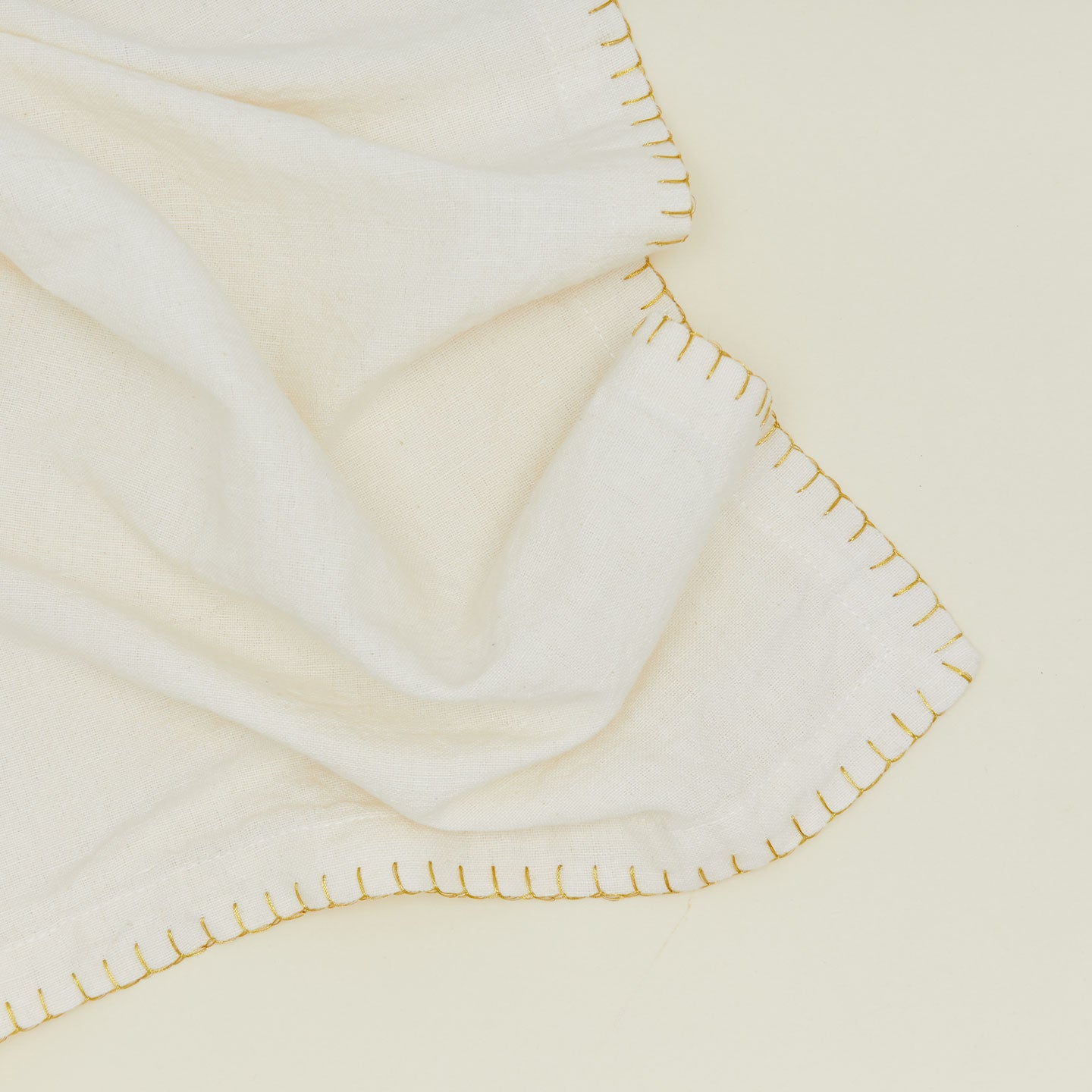 Close up of an ivory napkin with gold blanket stitching. 