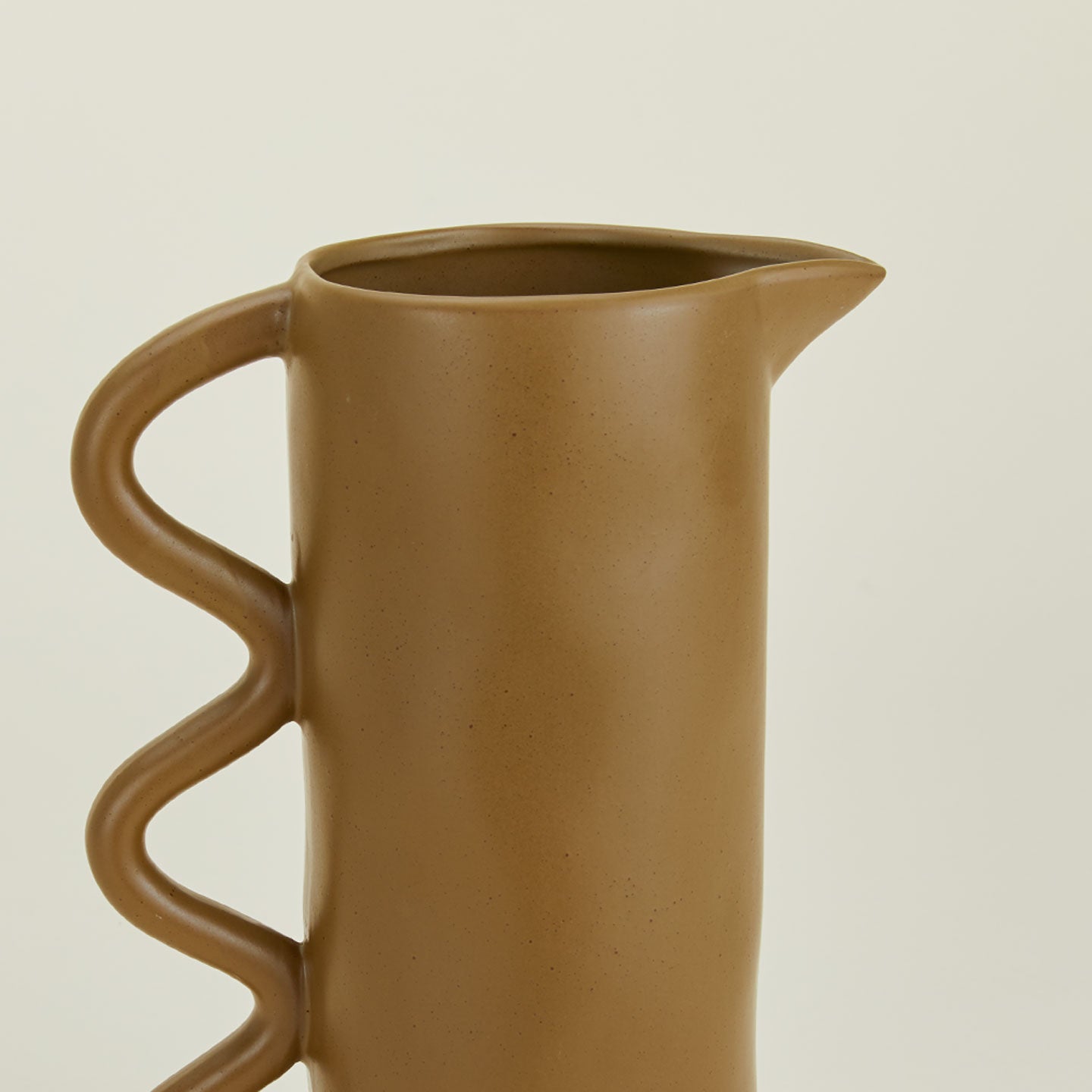 Close up of a stoneware pitcher with a wavy handle in bronze.