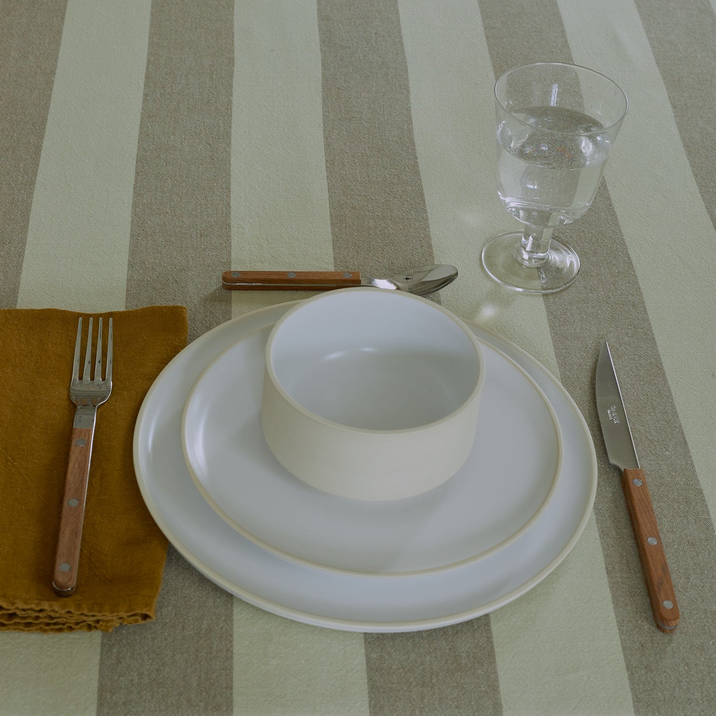 Placesetting with Modernist Cereal Bowl on ivory striped tablecloth.