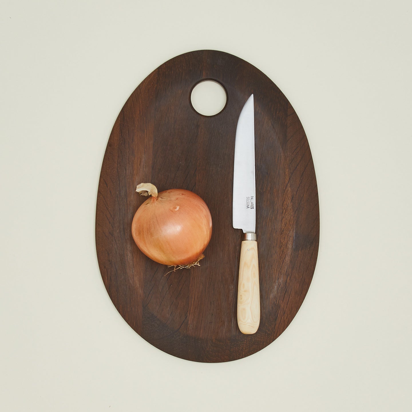 An overhead of a small knife on a walnut cutting board with an onion.