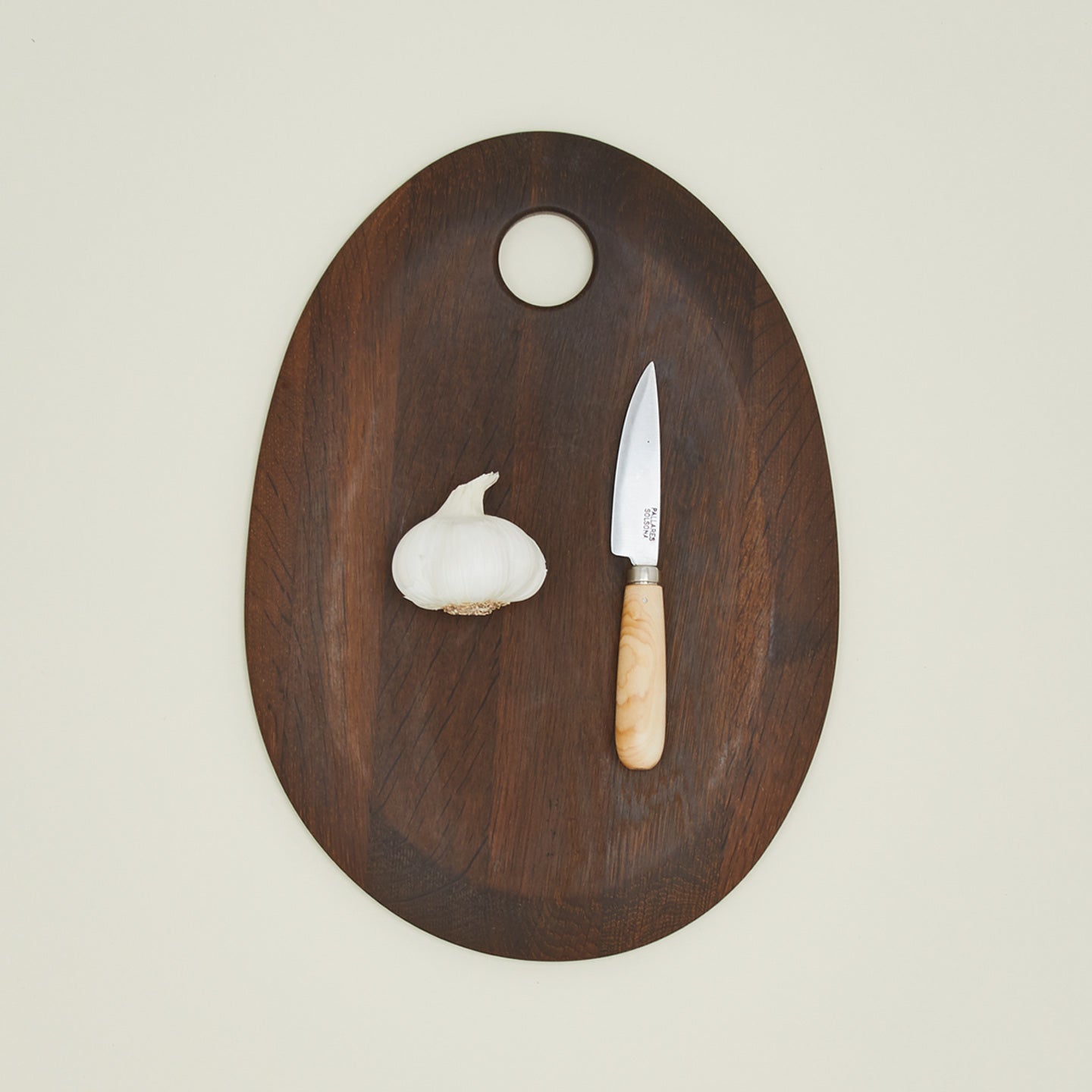 An overhead of a small knife on a walnut cutting board with garlic.