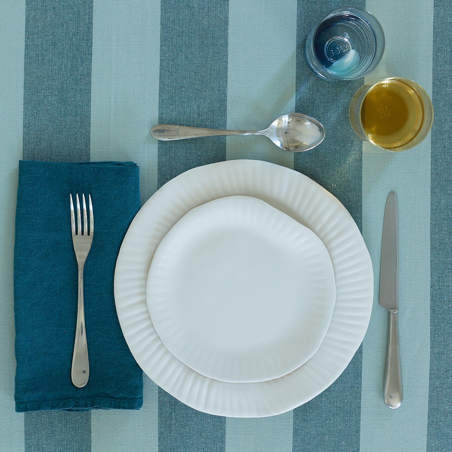 Placesetting with Porcelain Paper Plates on blue striped tablecloth.