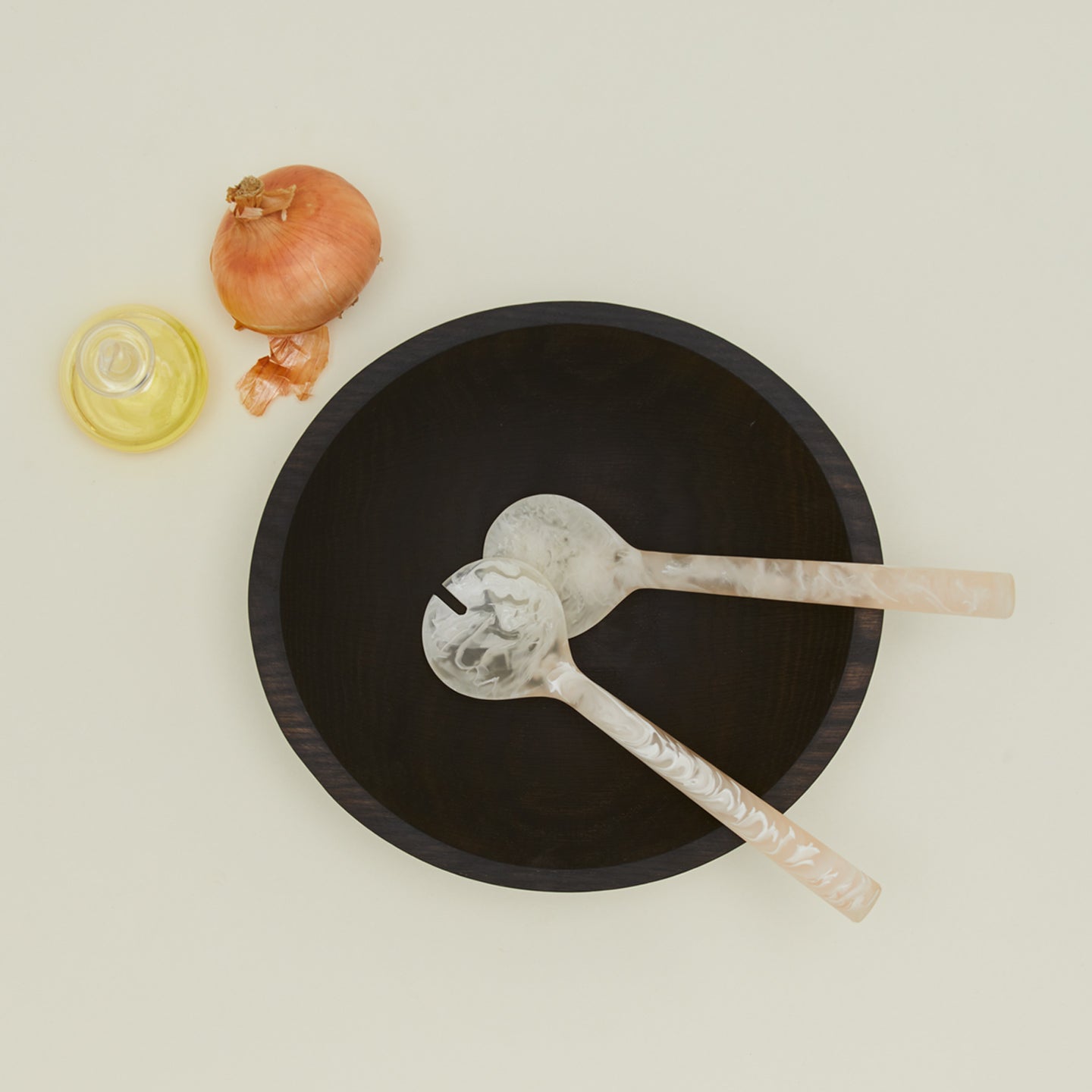 Flow resin salad servers with dark wooden bowl, onion, and a bottle of oil