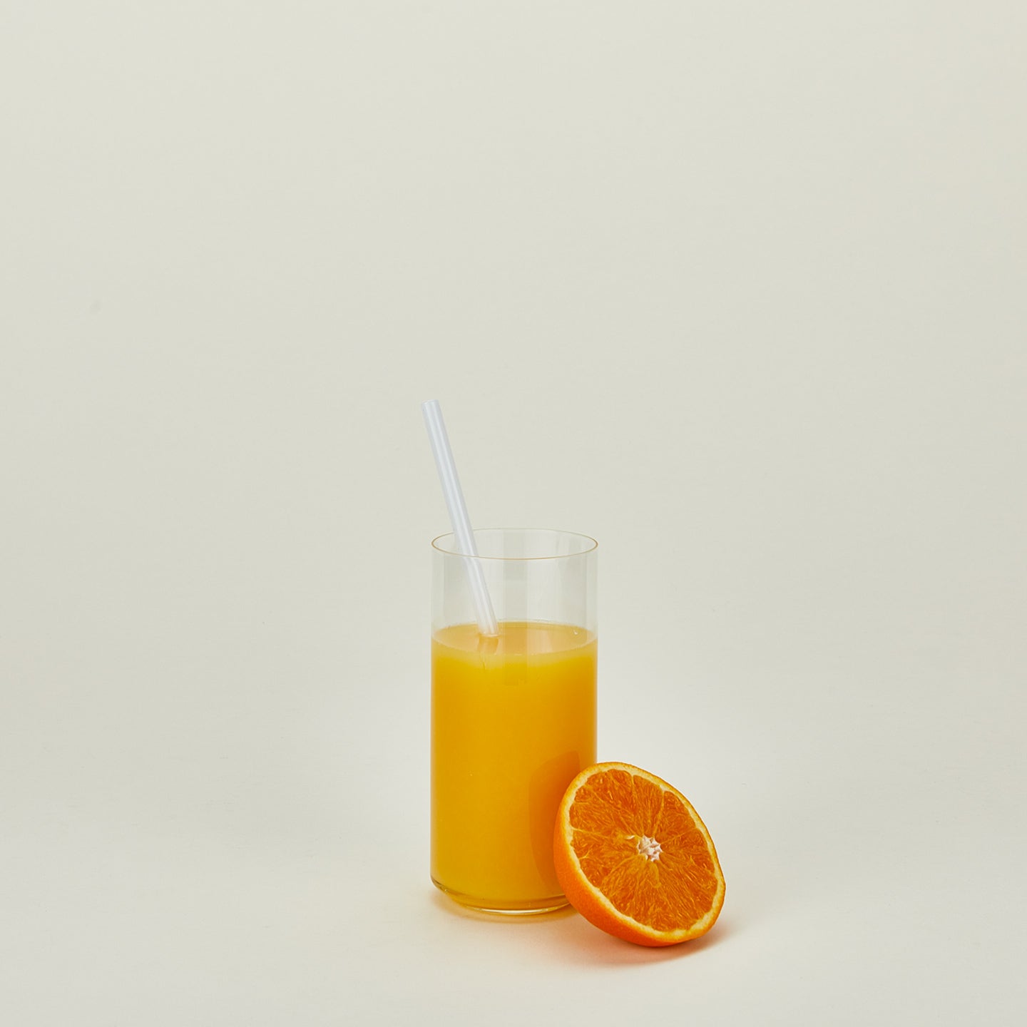 Simple glassware tall individual with orange juice, straw and orange half