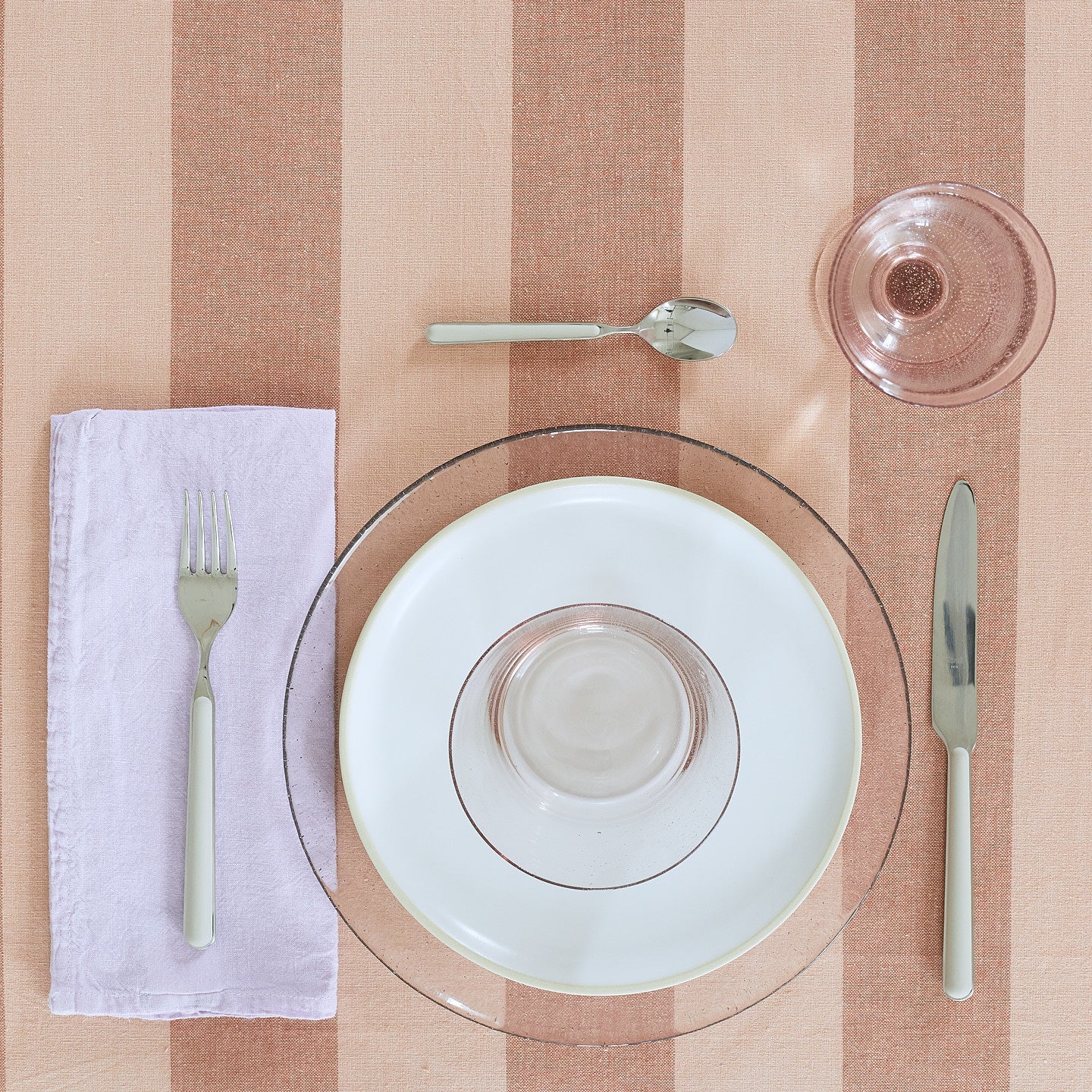 Place setting with a Simple Linen Napkin in Lilac on a pink striped tablecloth.