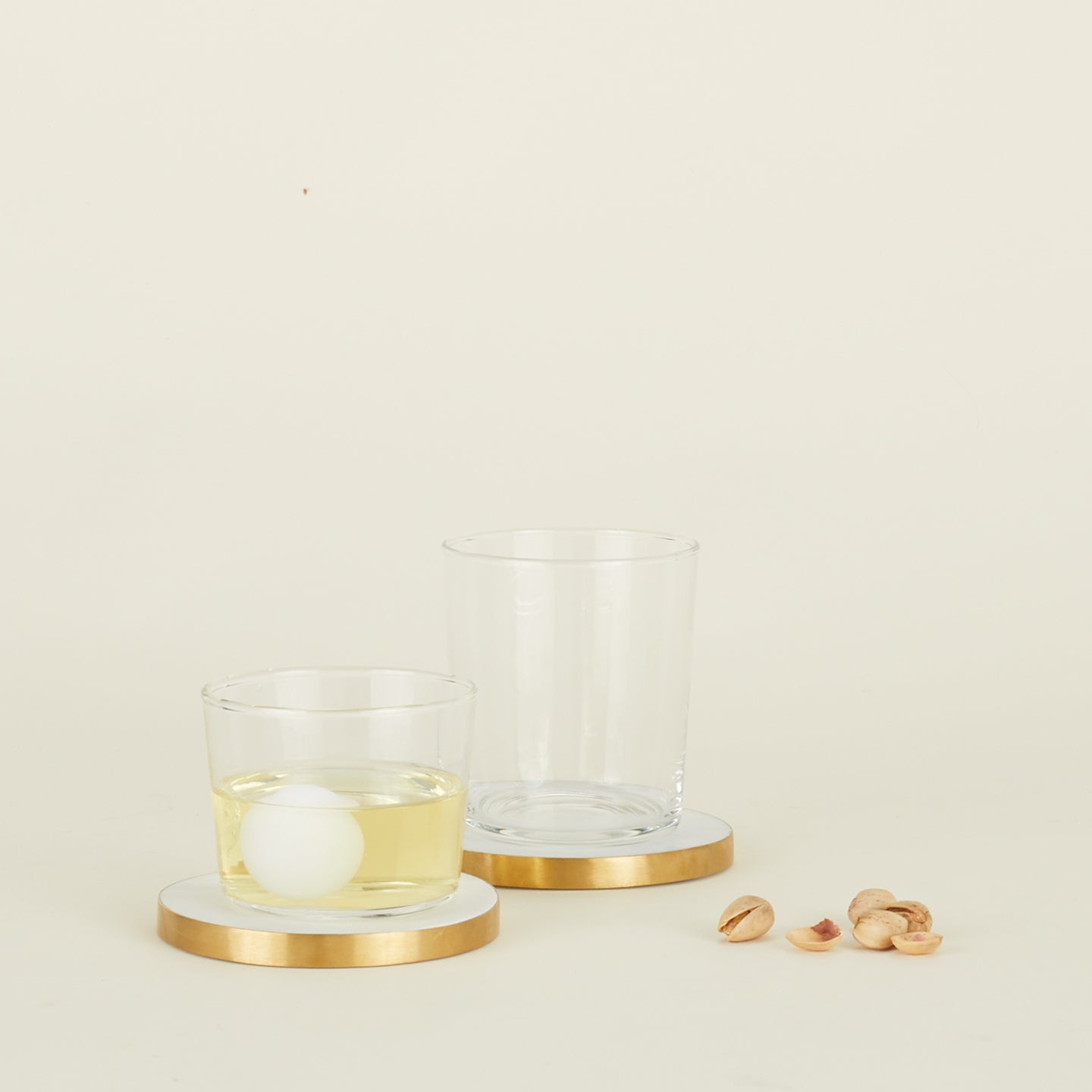 Two drinking glasses resting on Simple Marble Coasters with pistachios scattered nearby.