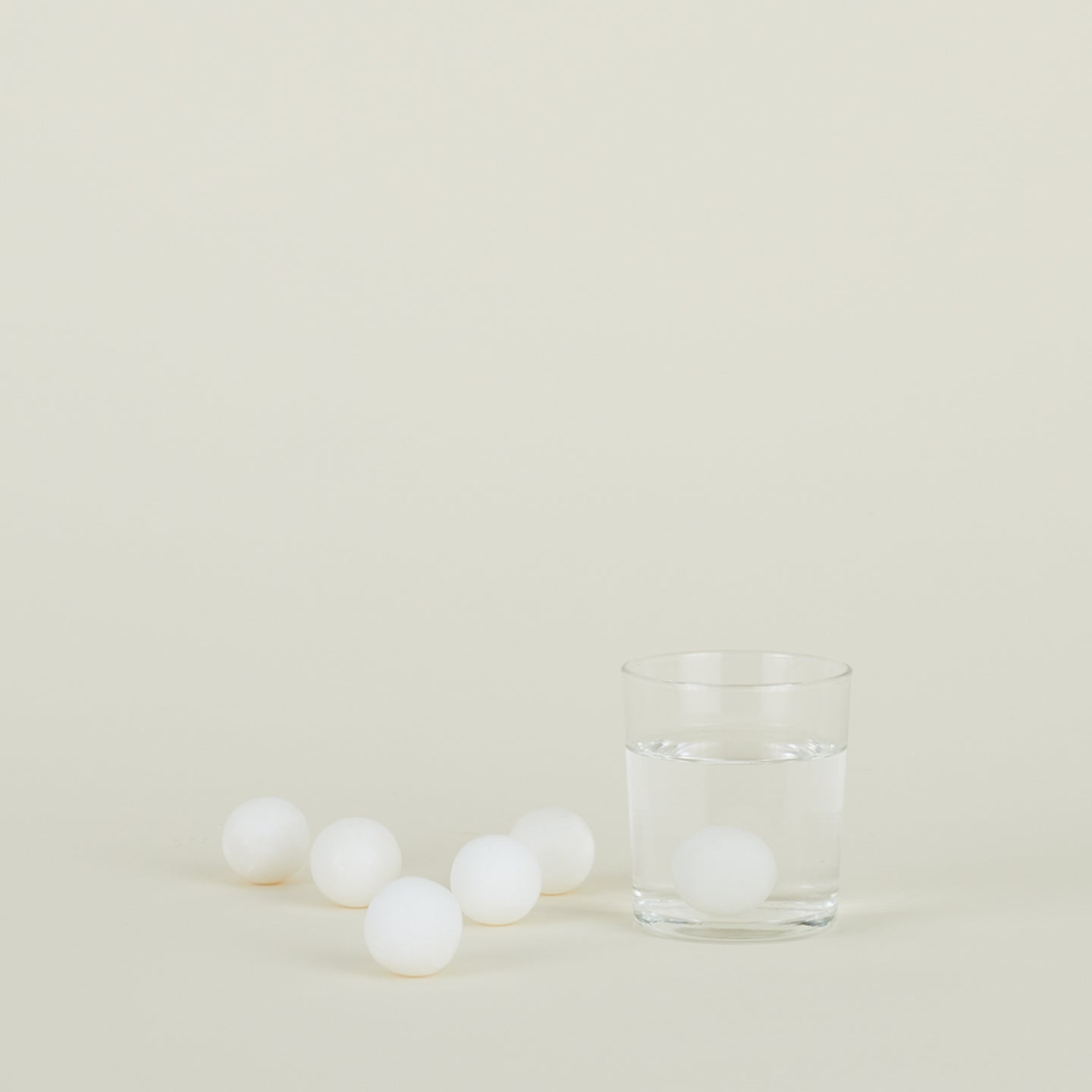 Drinking glass filled with water and a Simple Marble Drink Rock with several drink rocks scattered nearby.