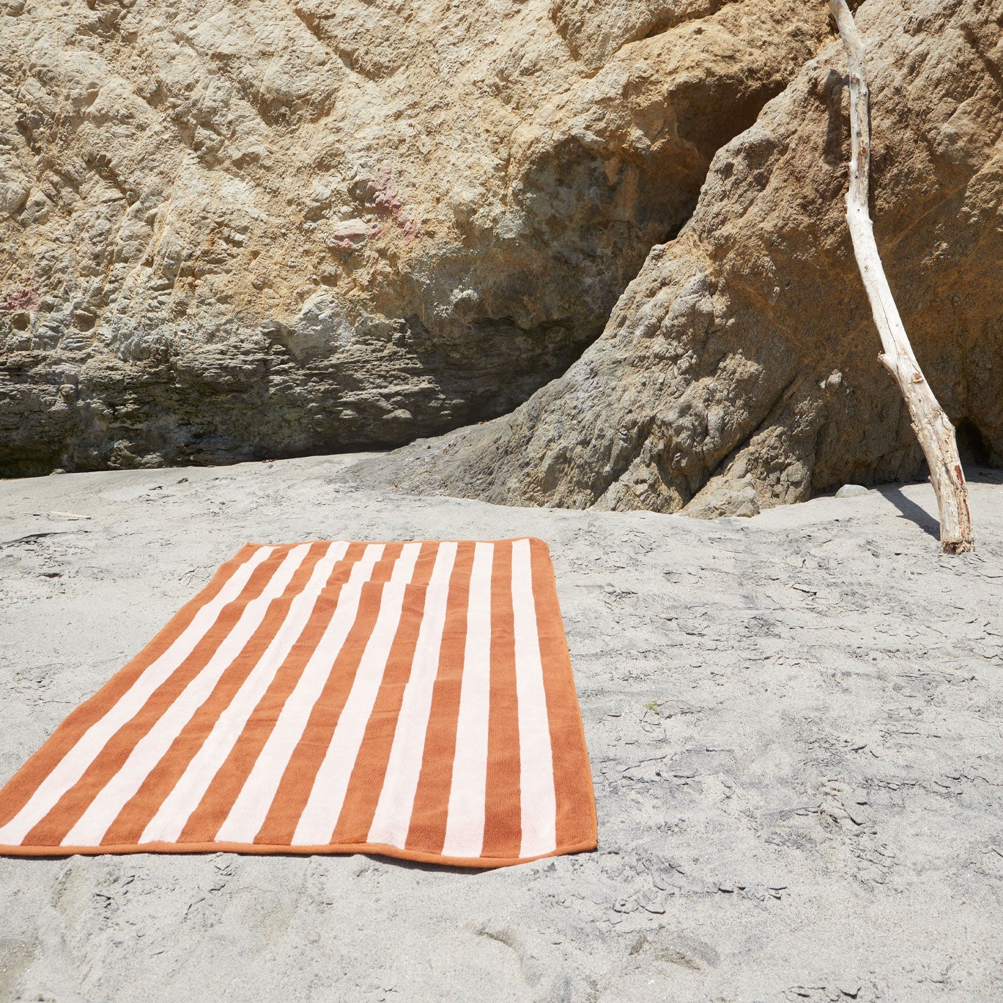 A striped blush and terracotta terry towel at the beach.