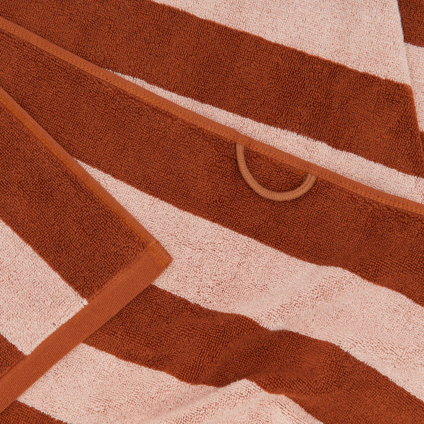 A close up of a striped blush and terracotta terry bath towel with a hanging loop.