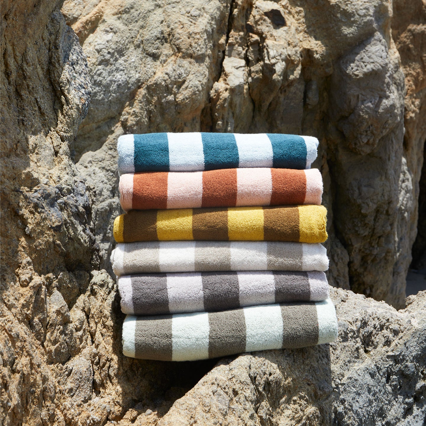 A stack of striped terry towels in six colors on a rock formation.
