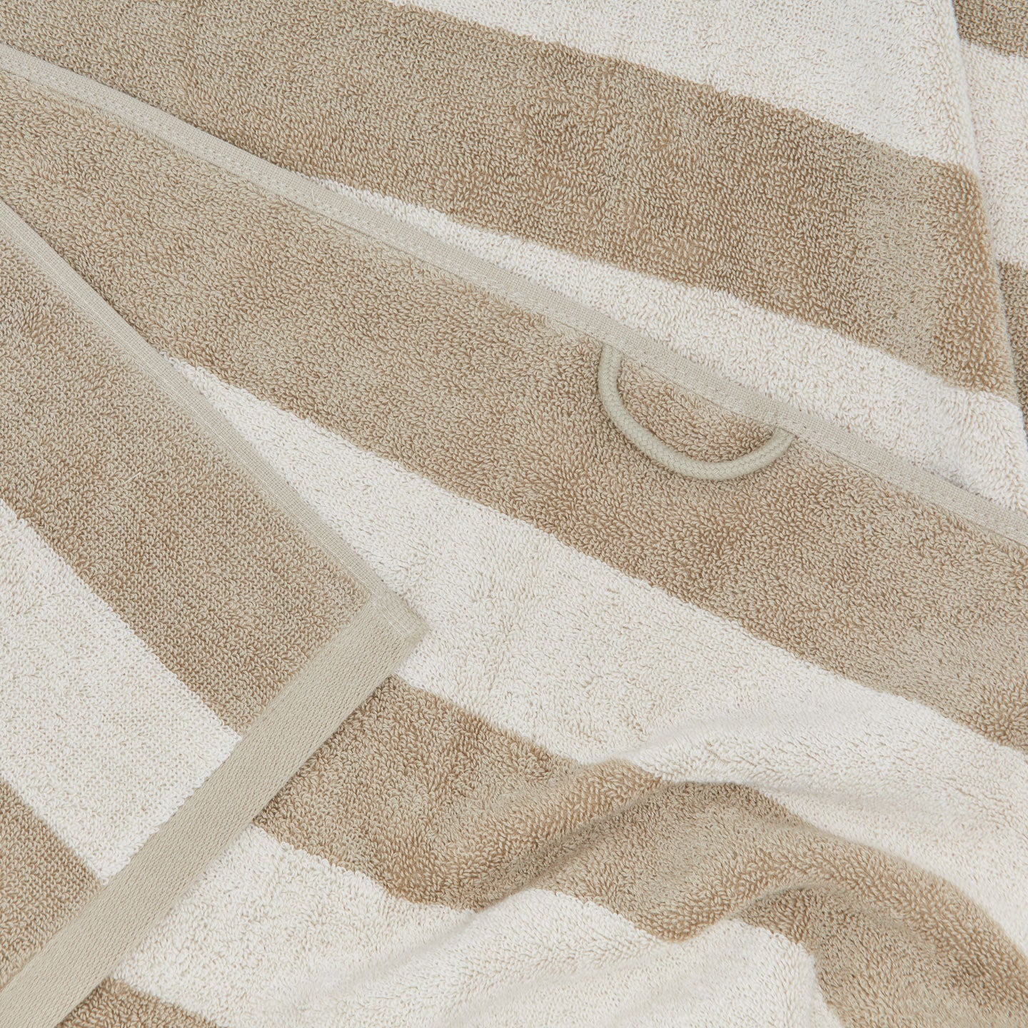 A close up of a striped ivory and flax terry bath towel with a hanging loop.