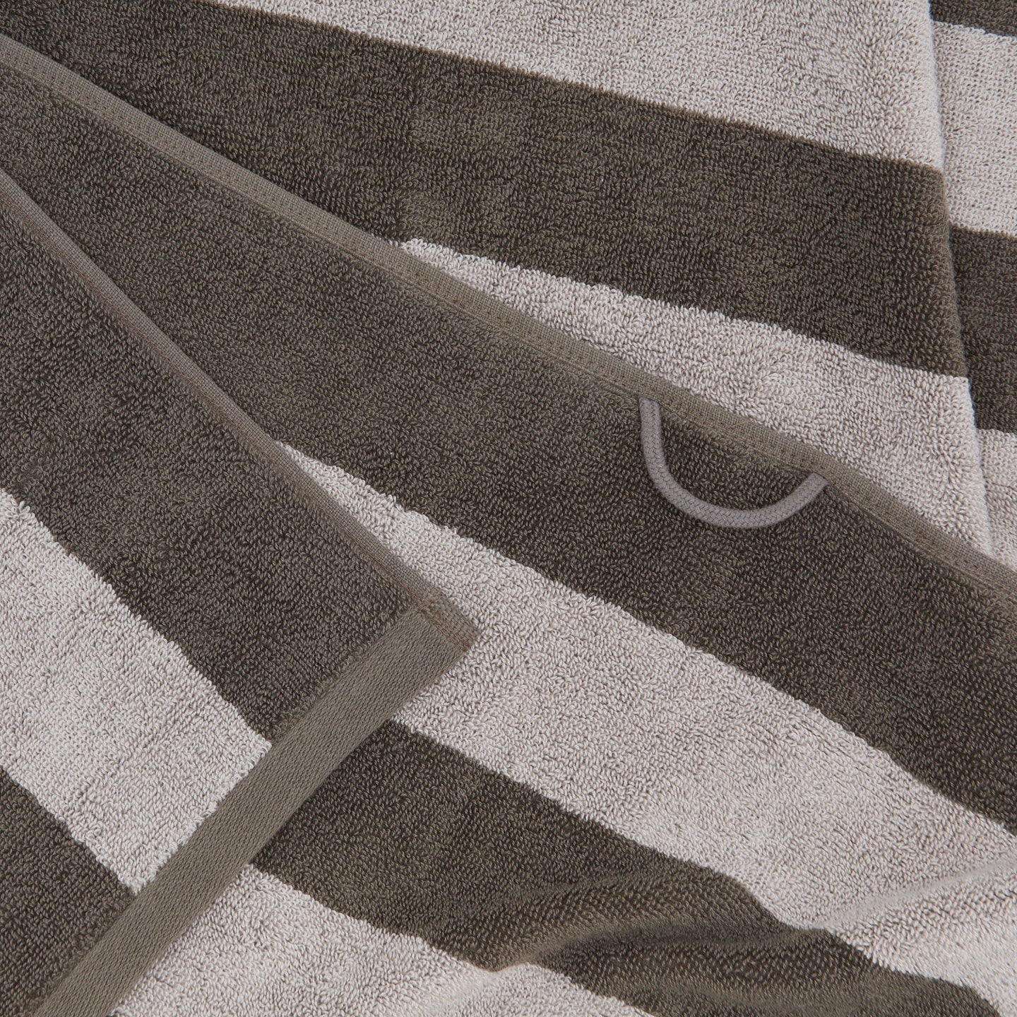 A close up of a striped light grey and dark grey terry bath towel with a hanging loop.