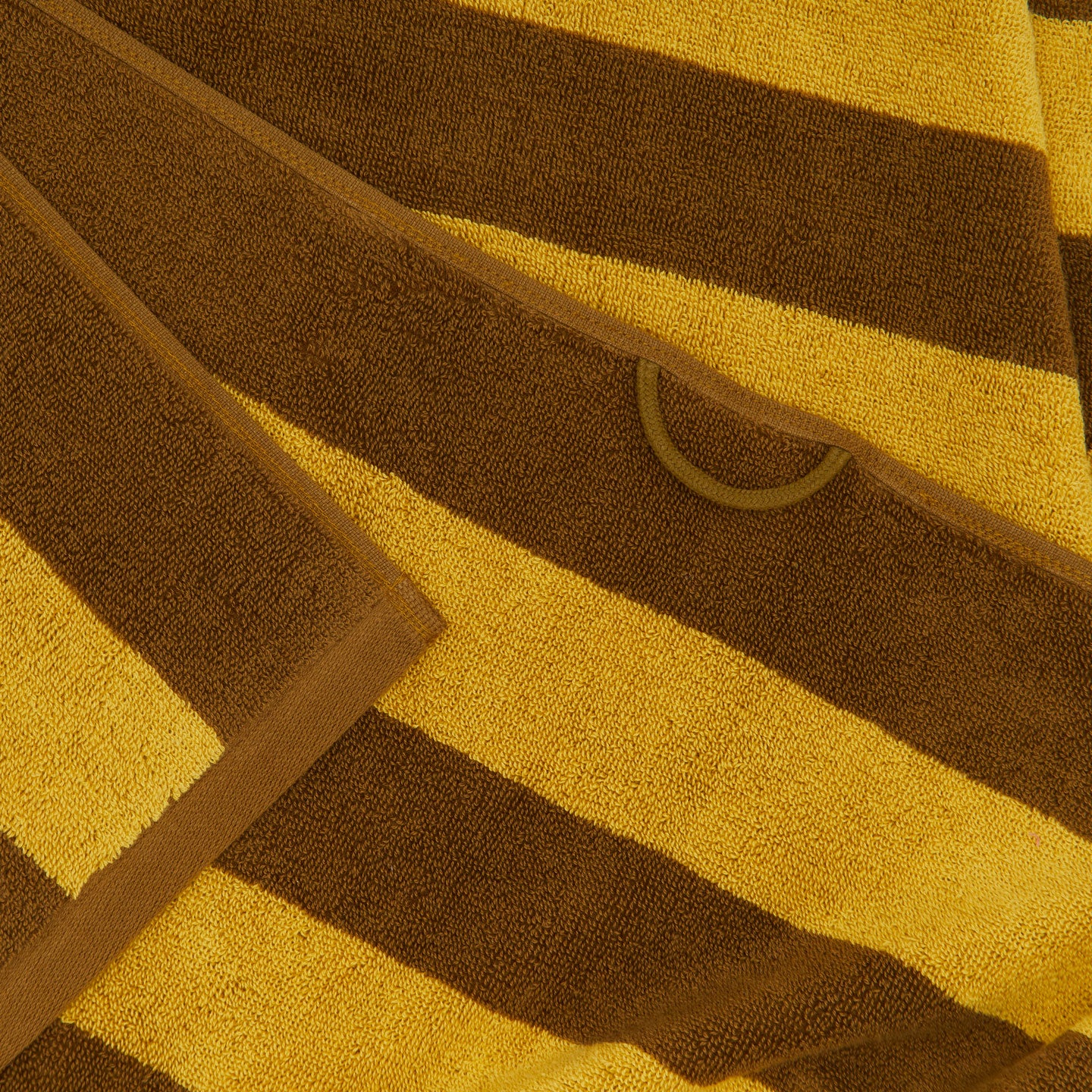 A close up of a striped mustard and bronze terry bath towel with a hanging loop.