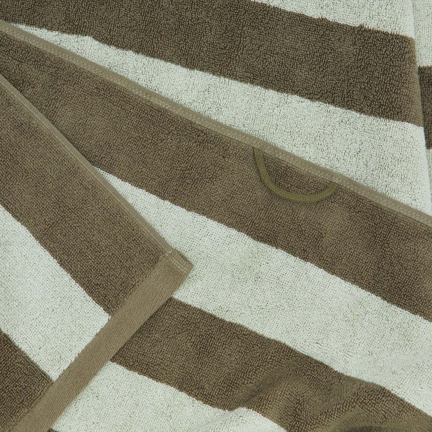 A close up of a striped olive and sage terry bath towel with a hanging loop.