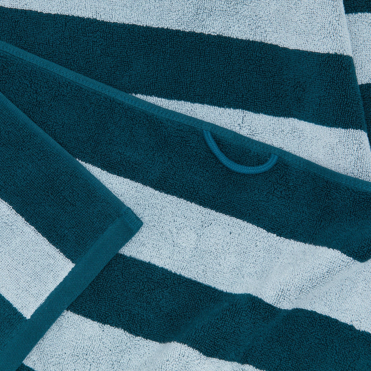 A close up of a striped sky and peacock terry bath towel with a hanging loop.