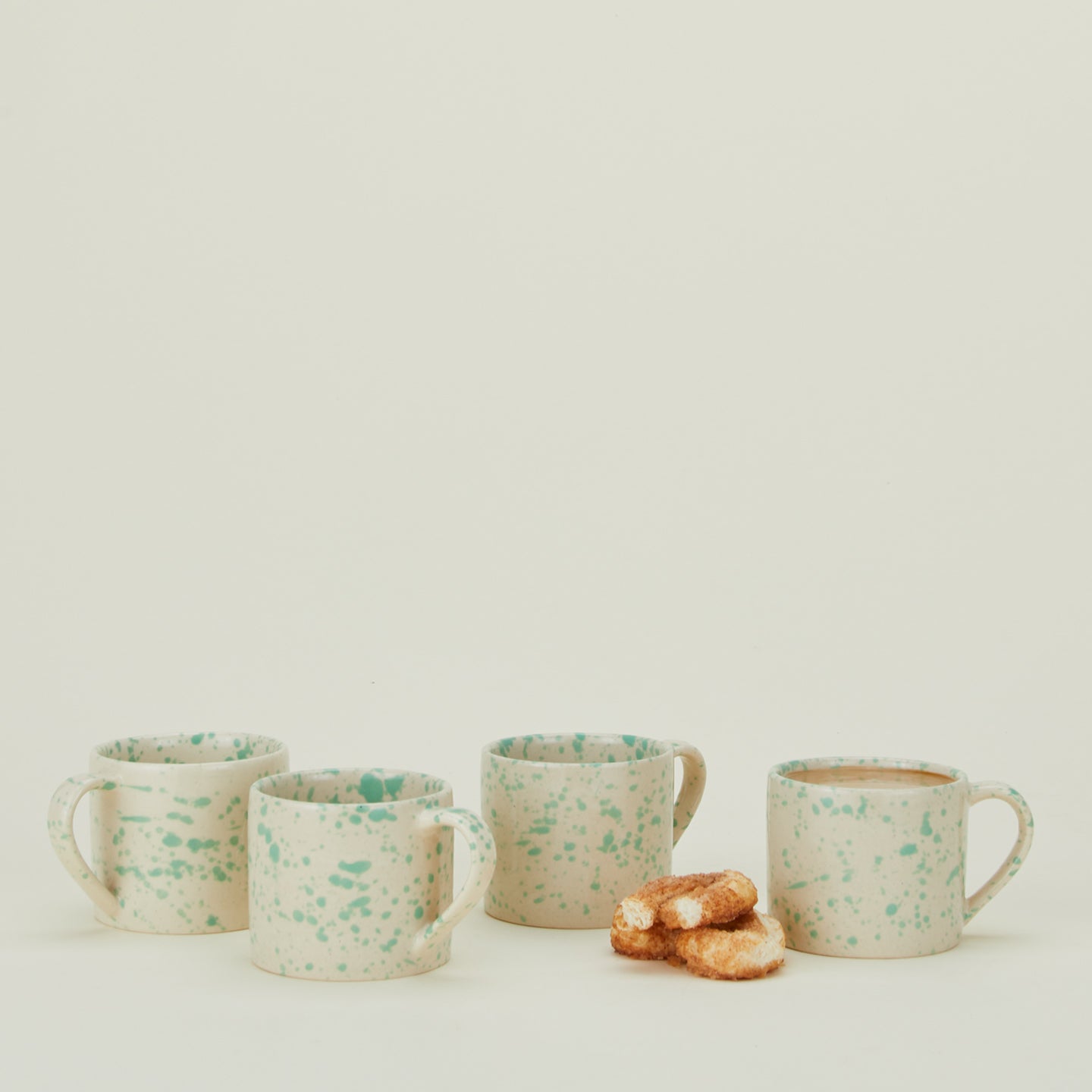 Set of four Splatterware mugs in Nettle with coffee and pastries.