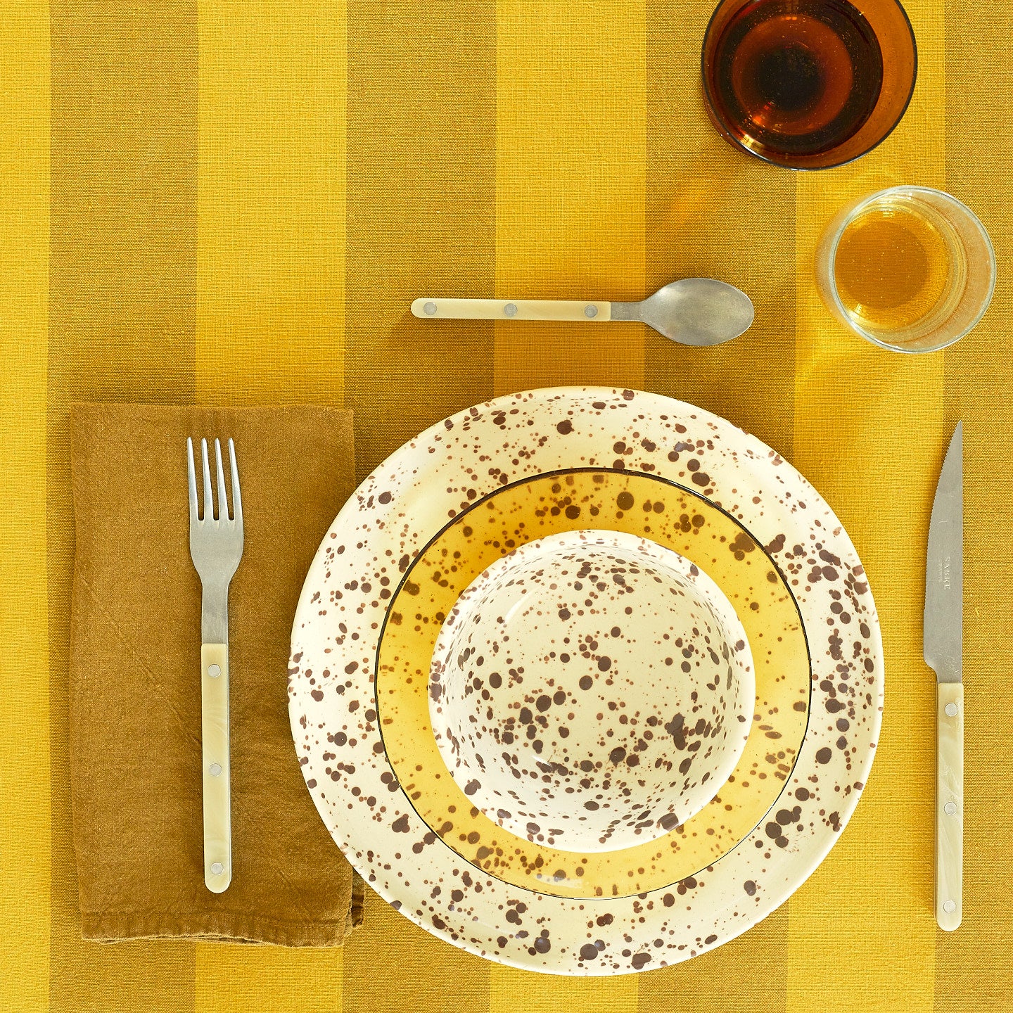 Place setting with Splatterware Bowl in Cacao on a yellow striped tablecloth.