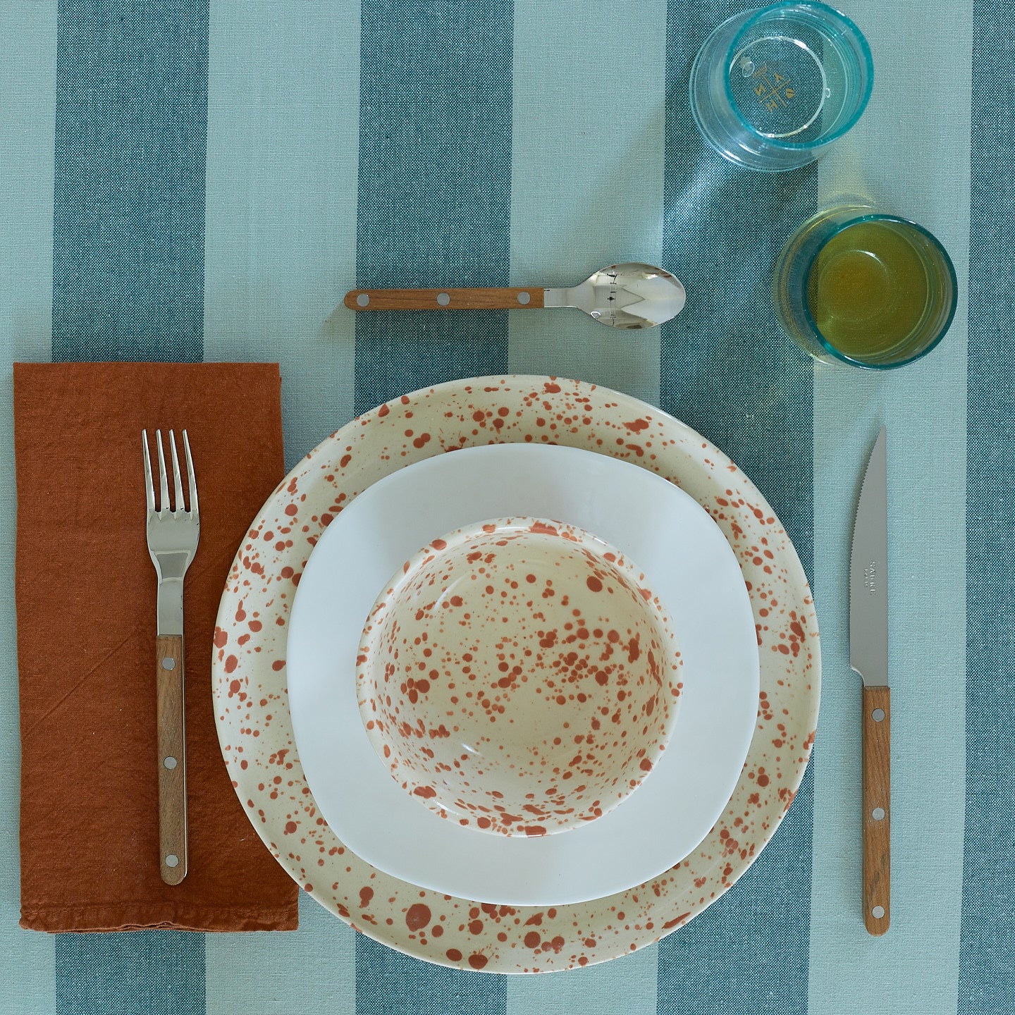 Place setting with Splatterware Bowl in Terra on a blue striped tablecloth.