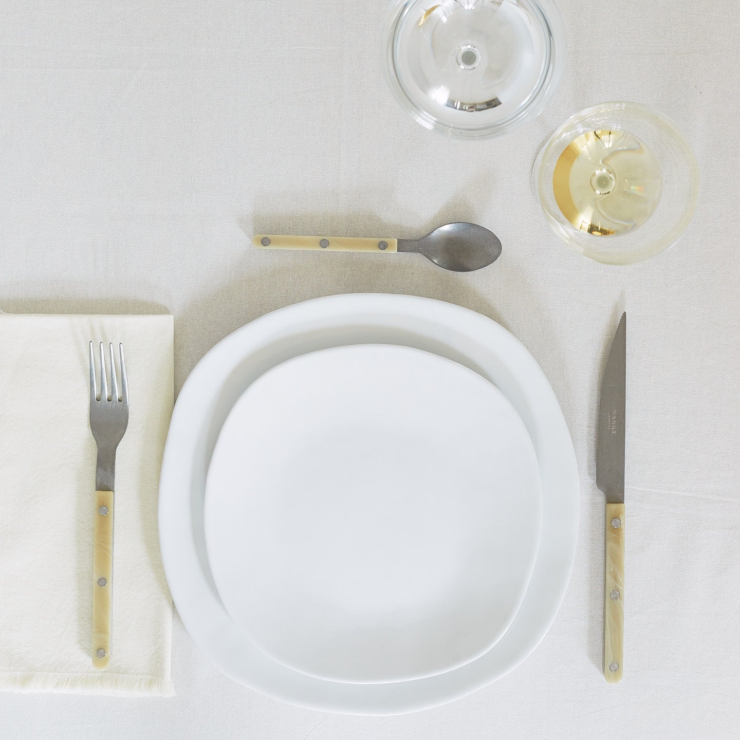 Placesetting of white Strata dinnerware on pink striped tablecloth.