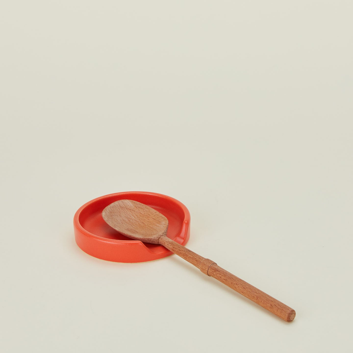 A paprika stoneware spoon rest with a wooden spoon.