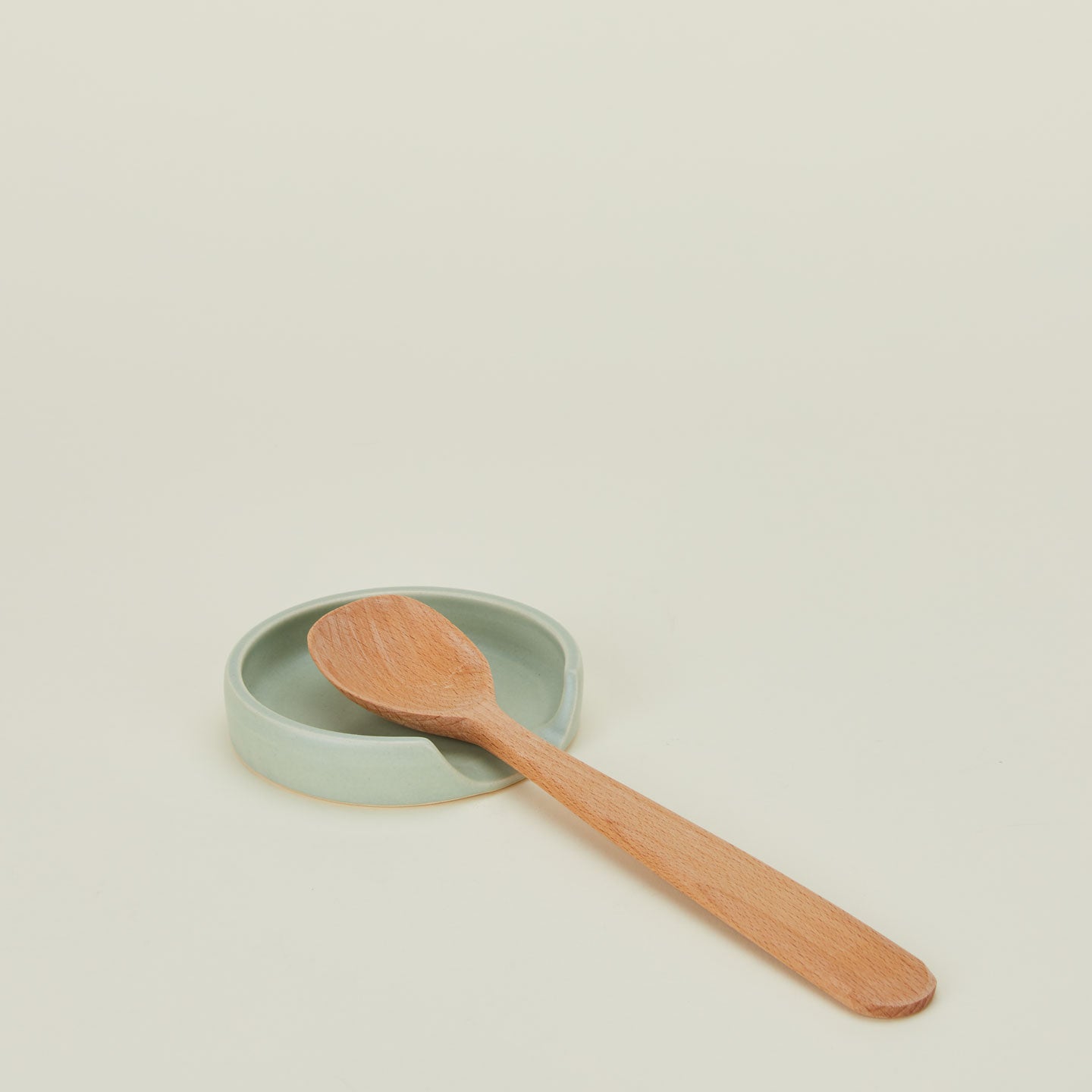 A seafoam stoneware spoon rest with a wooden spoon.