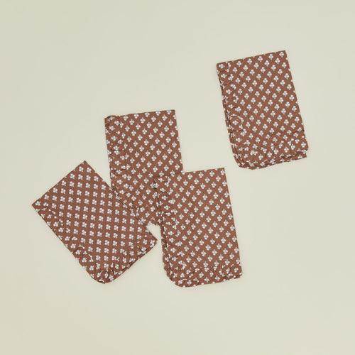 A set of four ruffled dinner napkins with a floral print in Constance brown.