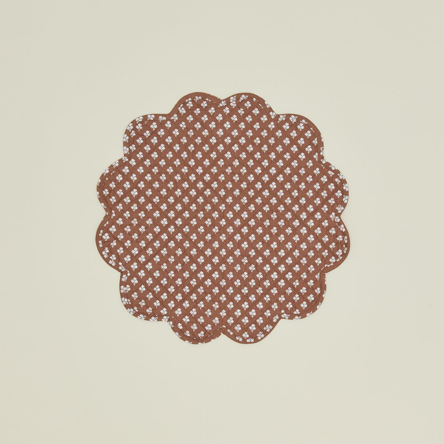 A round quilted placemat with a floral print in Constance brown.