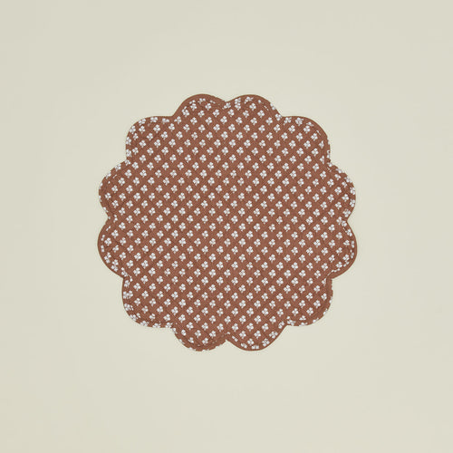 A round quilted placemat with a floral print in Constance brown.